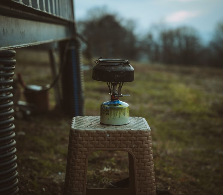 Gros plan d'un réchaud de camping sur un tabouret dans un cadre rural en plein air.
