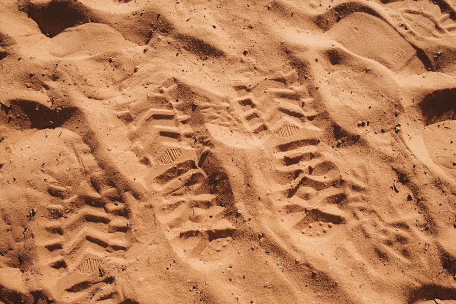 Empreintes détaillées sur le sable du désert, montrant des motifs de semelles dans un cadre chaleureux.