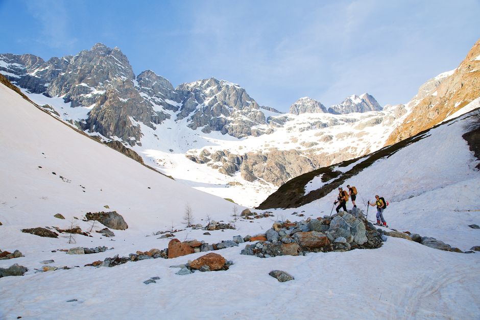 Des skieurs explorent le terrain enneigé des montagnes des Écrins en France sous un ciel d'hiver dégagé.