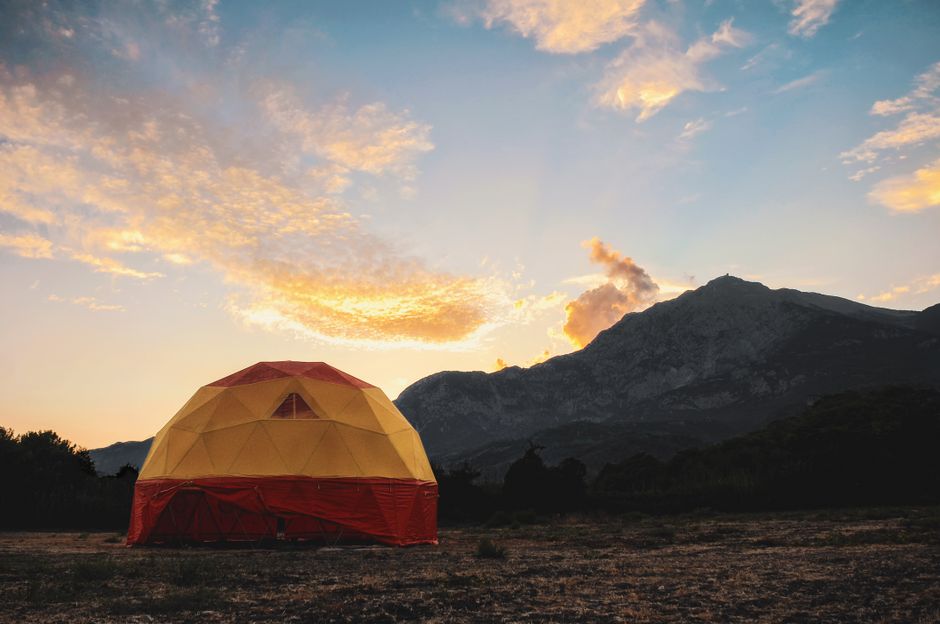 Tente géodésique sous un coucher de soleil vibrant avec des montagnes en arrière-plan.