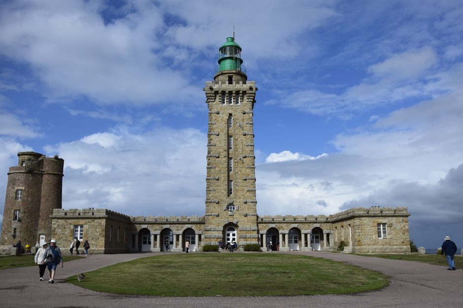 Le majestueux phare du cap Fréhel se dresse fièrement sous un ciel d'un bleu éclatant parsemé de nuages épars.