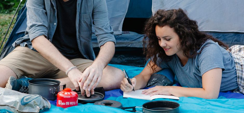 Un couple joyeux faisant du camping en plein air, écrivant des notes autour du matériel de camping dans une tente.