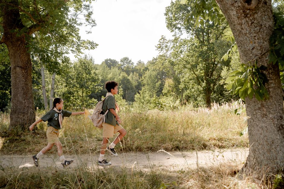 Deux enfants en uniformes de scout marchant le long d'un chemin forestier par une journée ensoleillée.
